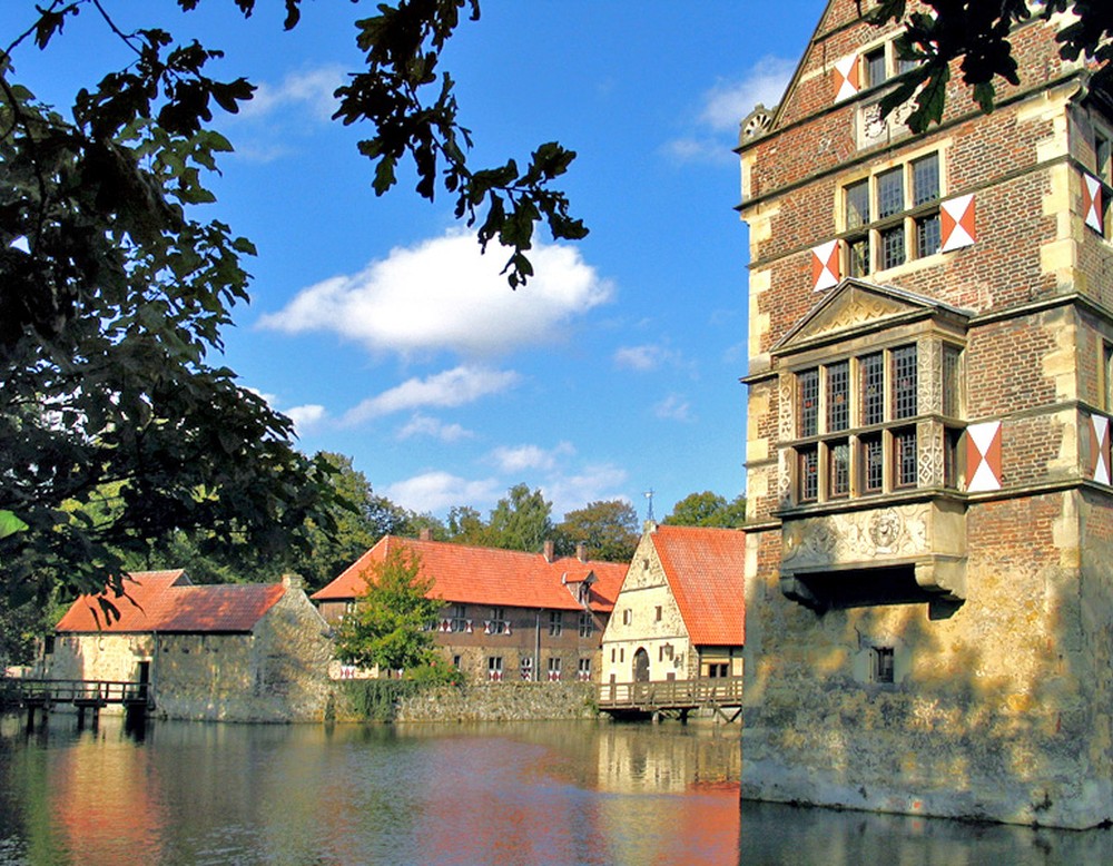 Blick über den Wassergraben entlang der Hauptburg auf die Vorburg. In das Bild ragen Äste eines Baumes hinein.