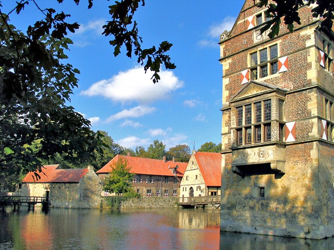 Blick über den Wassergraben entlang der Hauptburg auf die Vorburg. In das Bild ragen Äste eines Baumes hinein.