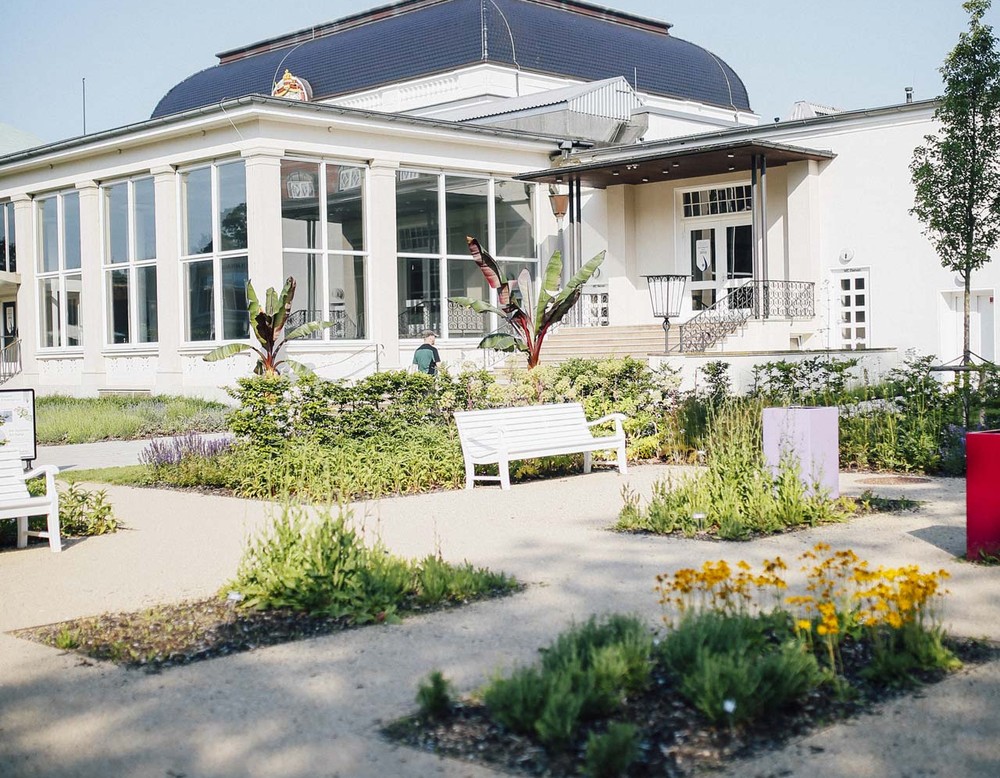 Blick auf das Kur- und Stadttheater am Kurpark Bad Salzuflen. Vor dem Gebäude befinden sich Blumenbeete und Bänke.