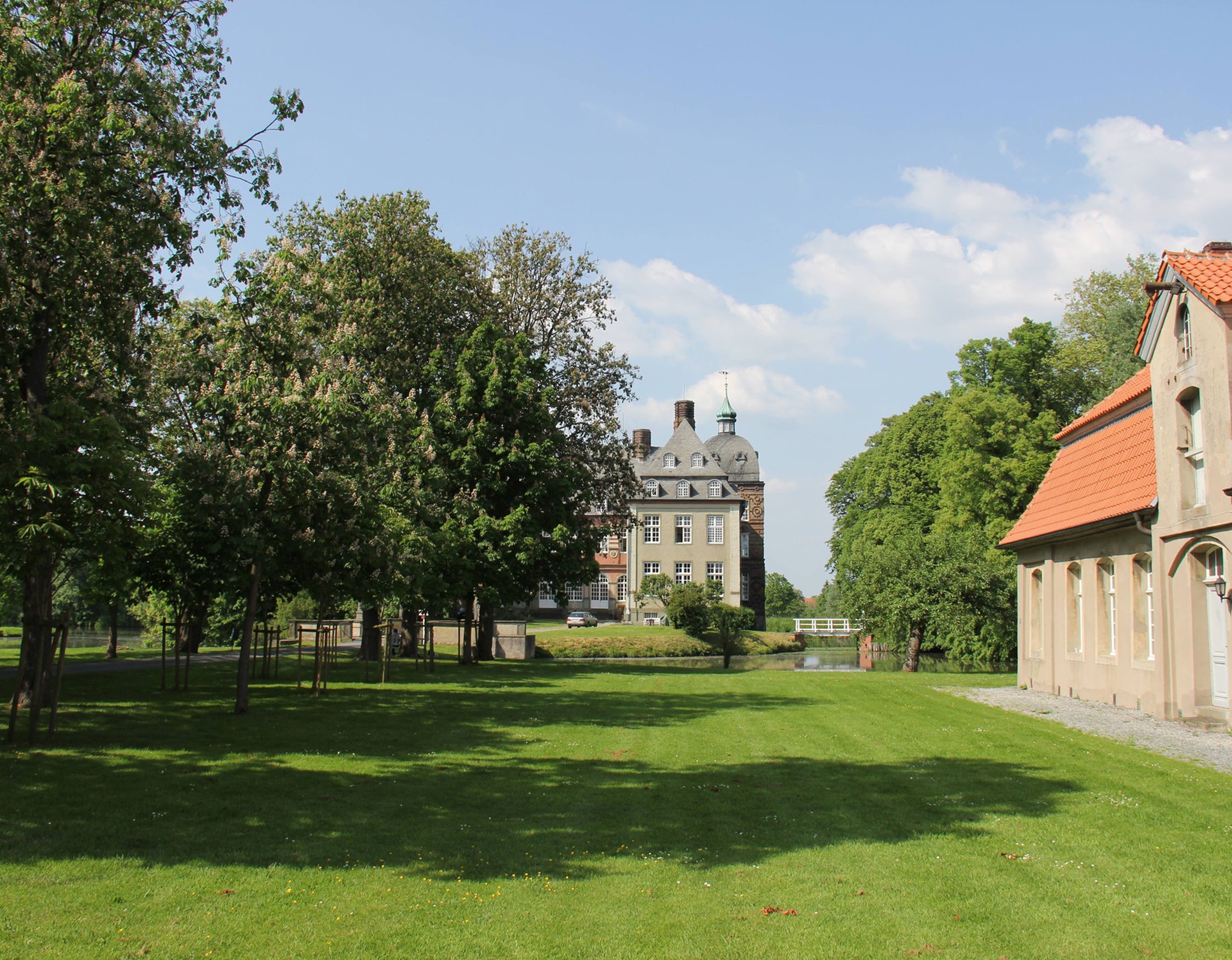 Blick von der Vorburg auf das Schloss Hovestadt. Rechts steht eines der einstöckigen Wirtschaftsgebäude. Durch die Vorburg führt eine Kastanienallee zum Schloss.
