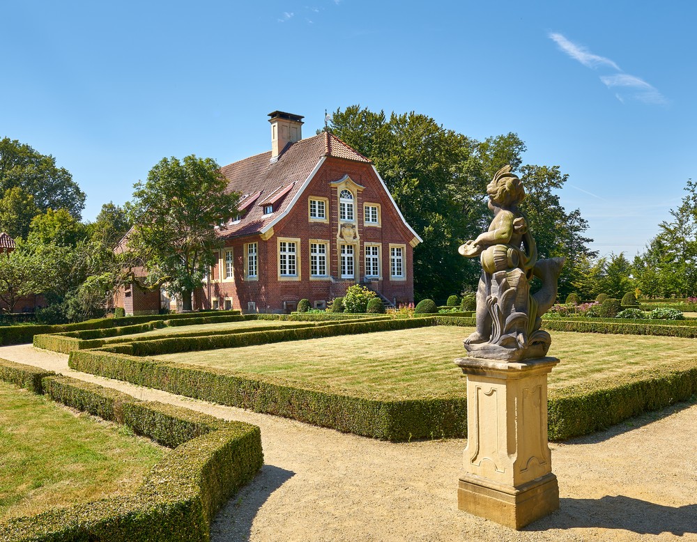 Die Gartenseite des Hauses Rüschhaus bei Münster. Davor befinden sich Wiesen, welche von Hecken umrandet sind.