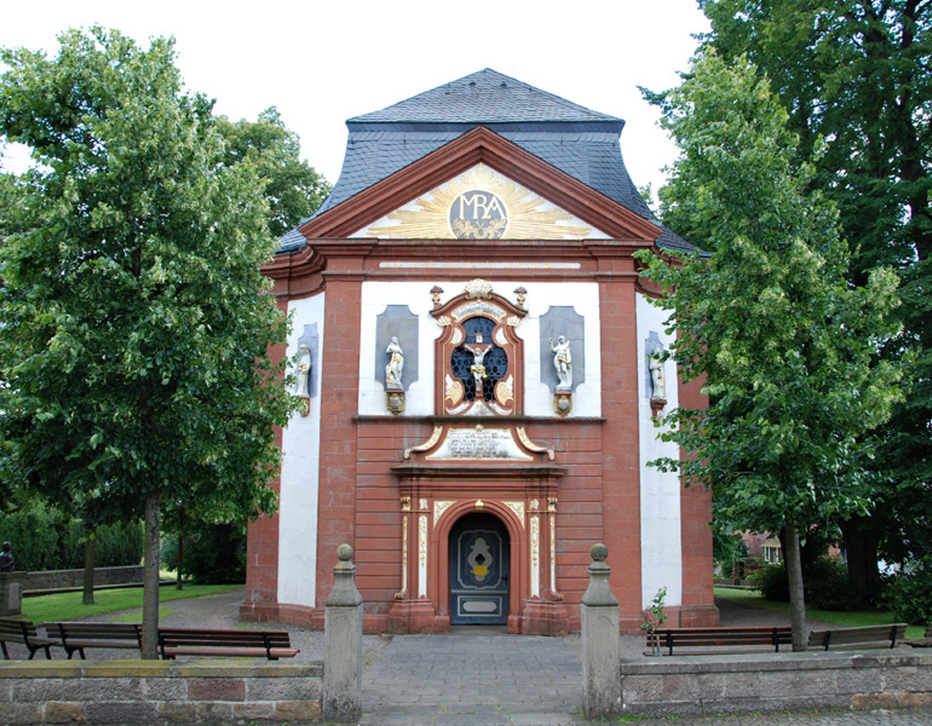 Blick auf die Wallfahrtskirche Mariä Heimsuchung. Über dem Eingang befindet sich ein Kruzifix aus Sandstein vor einem Fenster. Seitlich davon befinden sich Figuren.