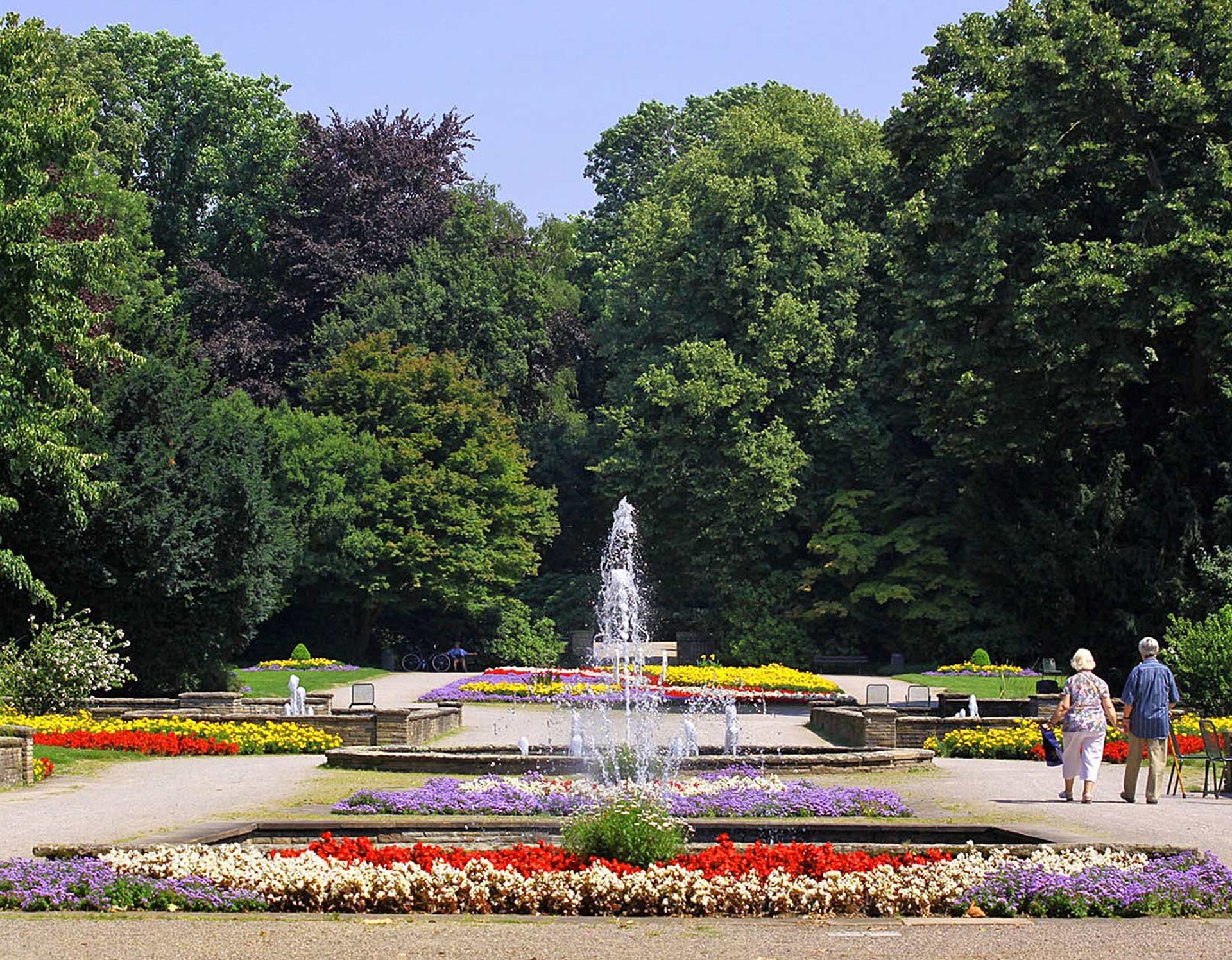 Mehrere Springbrunnen im Stadtgarten Gelsenkirchen. Drum herum sind Blumenbeete angelegt.