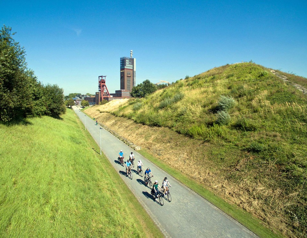 Unterhalb der Aussichtsplattform auf der Halde führt ein Weg entlang. Auf diesem befindet sich eine Gruppe Radfahrer.