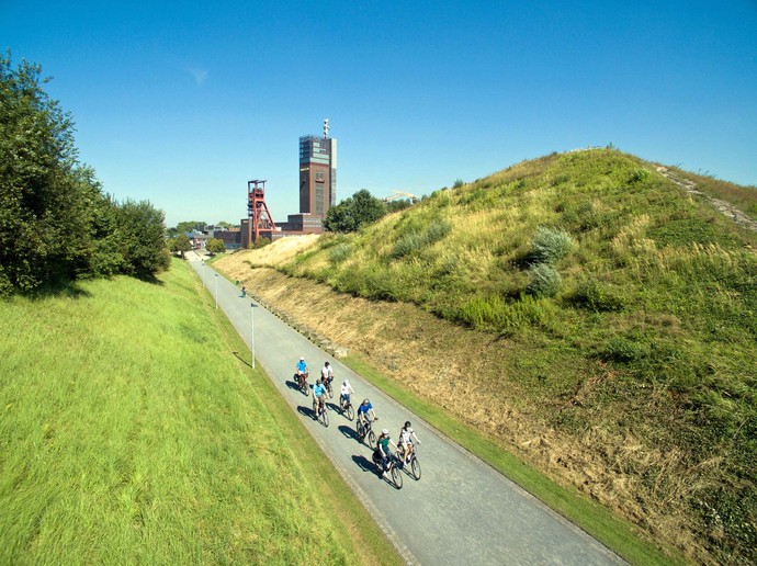 Unterhalb der Aussichtsplattform auf der Halde führt ein Weg entlang. Auf diesem befindet sich eine Gruppe Radfahrer.