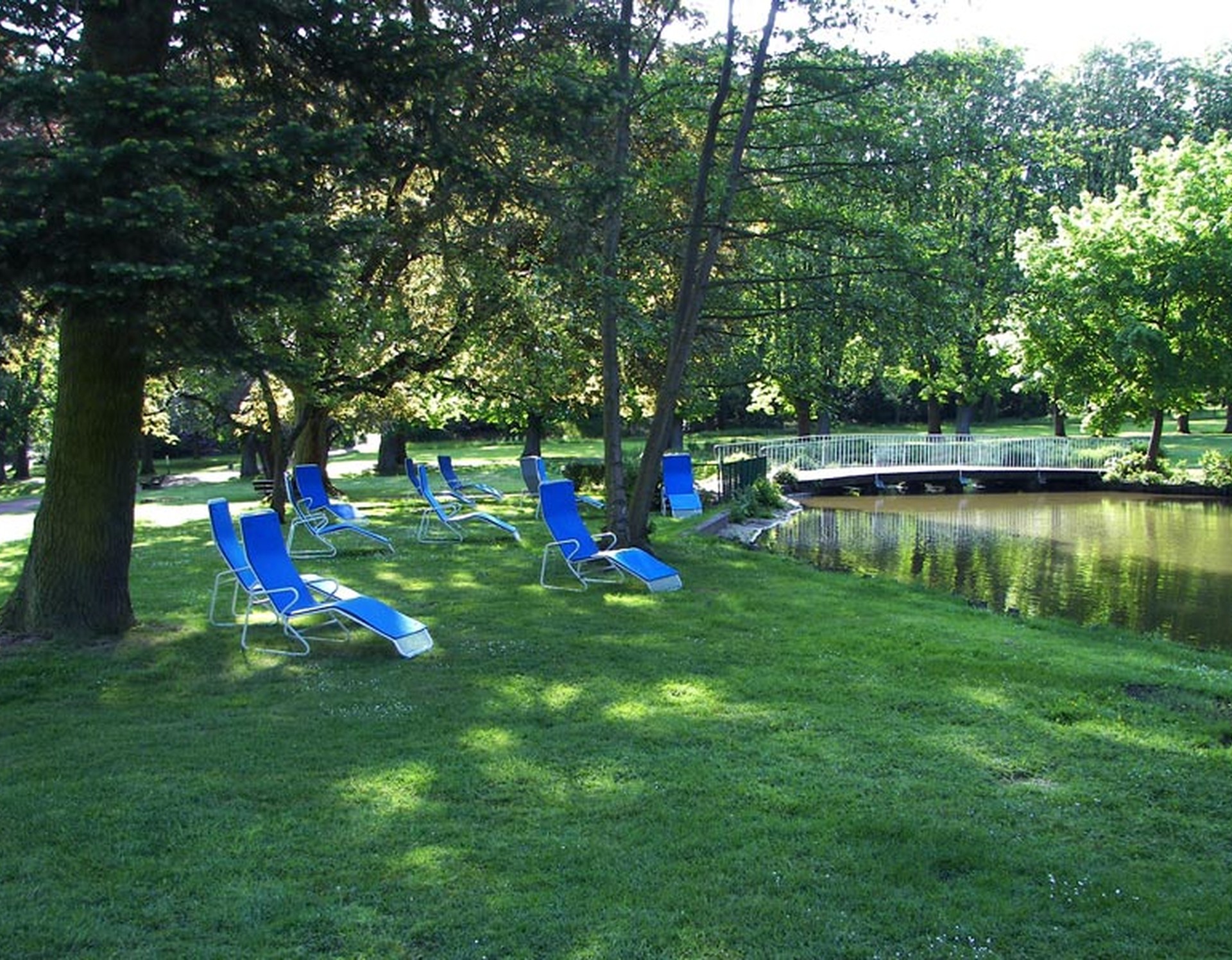 Blaue Liegestühle im Kurpark Bad Hermannsborn. Rechts führt eine Brücke über einen der Teiche im Park.