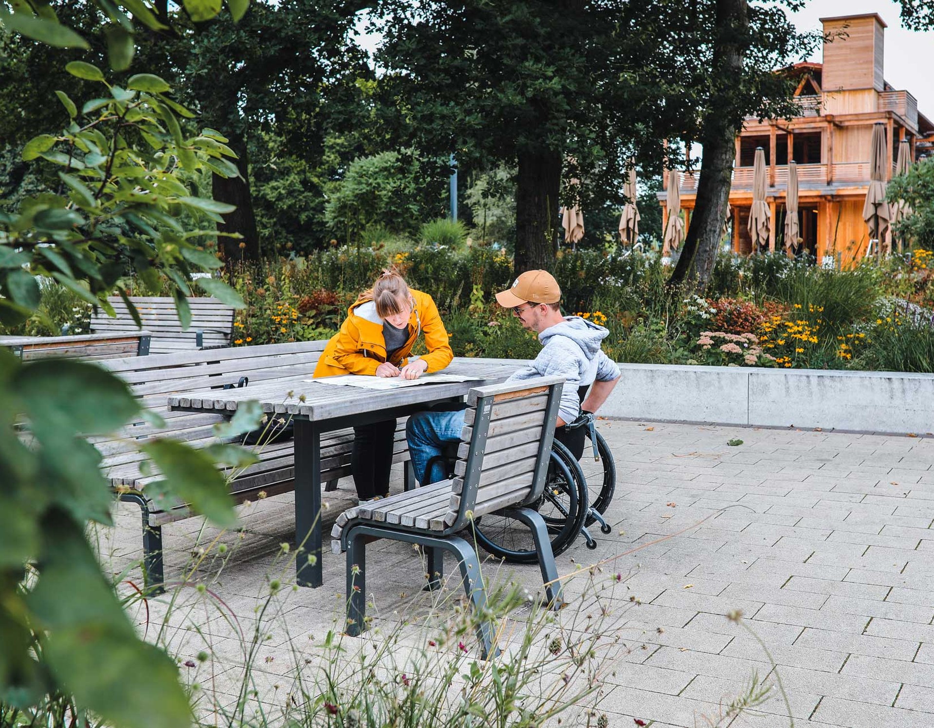 Zwei Menschen sitzen an einem der Sitzplätze mit Tischen im Kurpark Bad Sassendorf. Sie schauen gemeinsam in eine Karte.