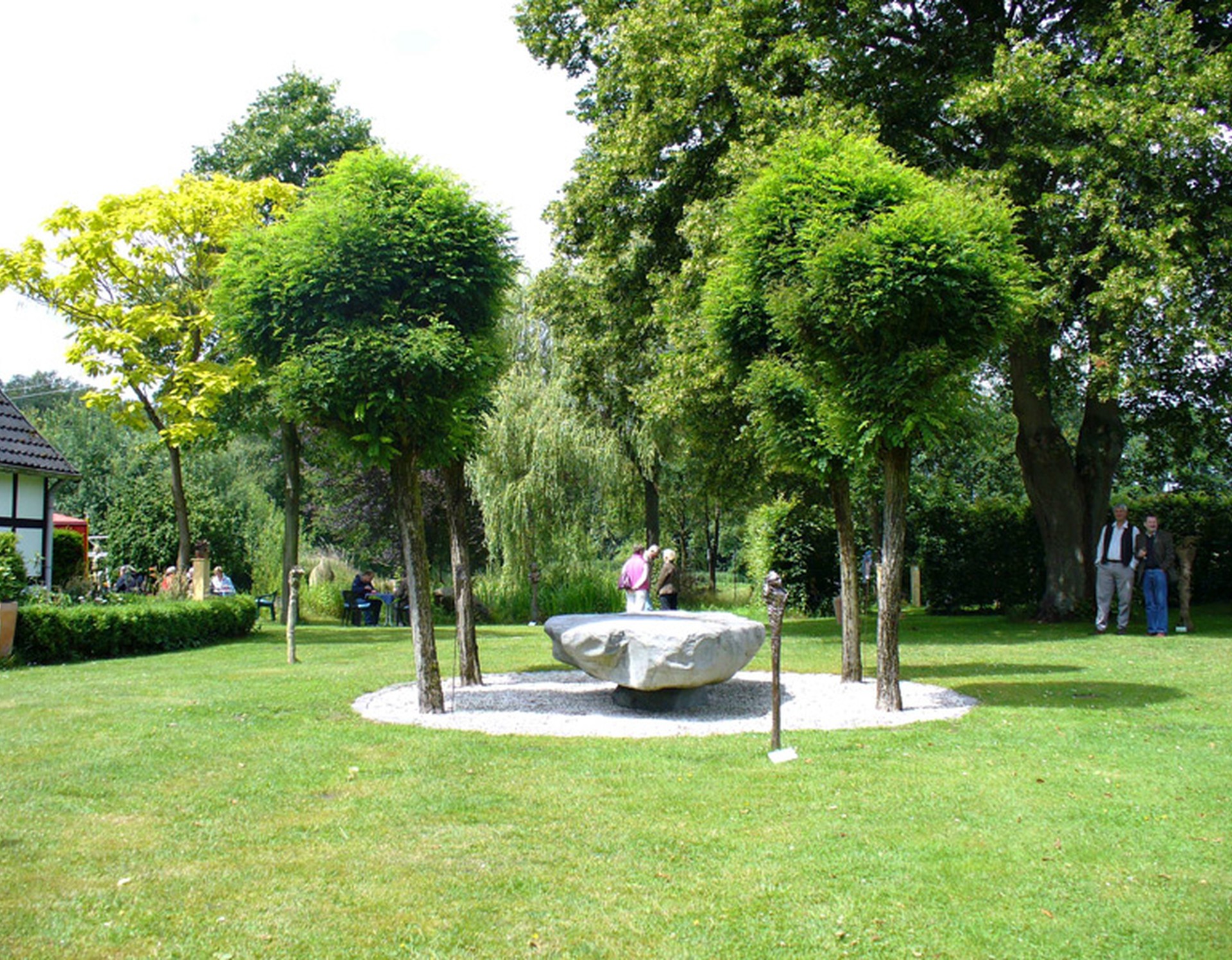 Eine steinerne Skulptur im Eventgarten des Heckentheaters. Diese ist von vier Bäumen umgeben.