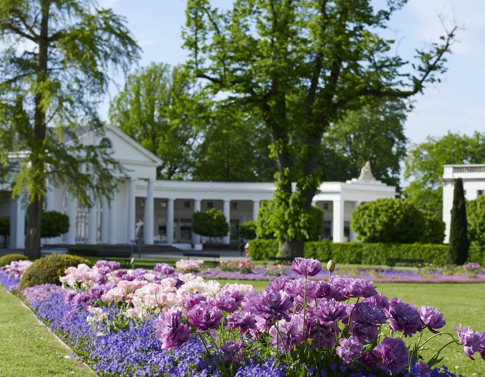 Blick über Blumenbeete hinweg auf die Wandelhalle im Kurpark Bad Oeynhausen. Sie ist in Form eines sechssäuligen ionischen Tempels errichtet worden.