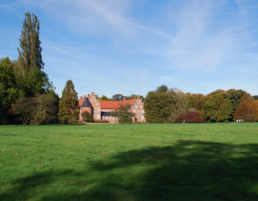 Eine weitläufige Wiese im Schlosspark. Im Hintergrund steht das Schloss Herten.