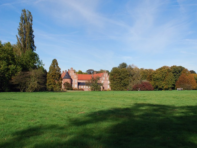 Eine weitläufige Wiese im Schlosspark. Im Hintergrund steht das Schloss Herten.