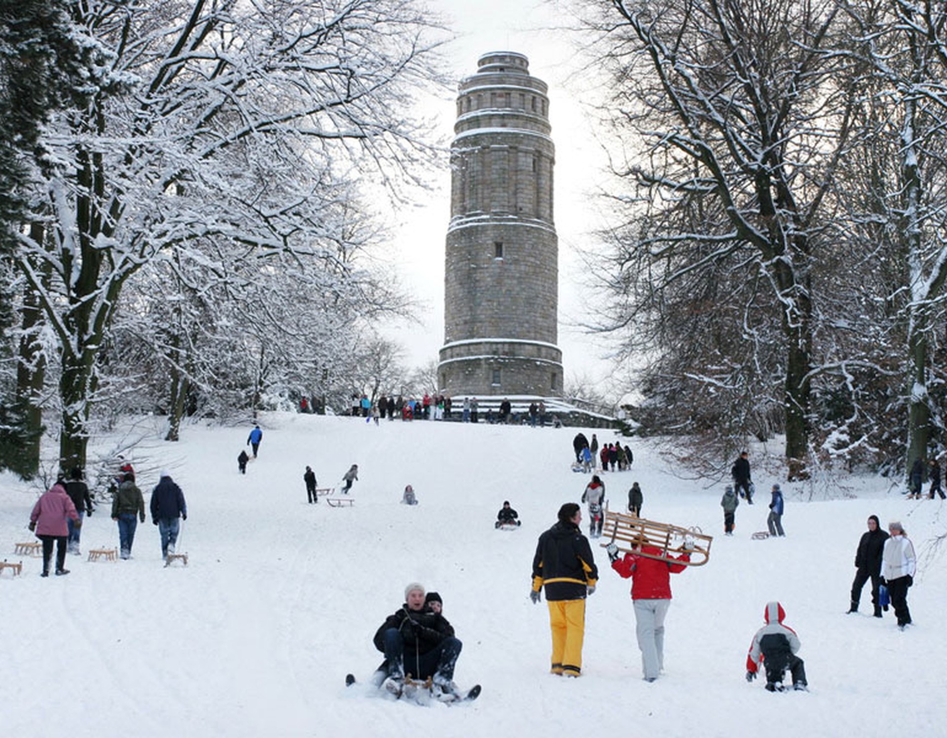 Der Bismarckturm im Stadtpark Bochum im Winter. Zahlreiche Menschen nutzen den Schnee zum Schlittenfahren.