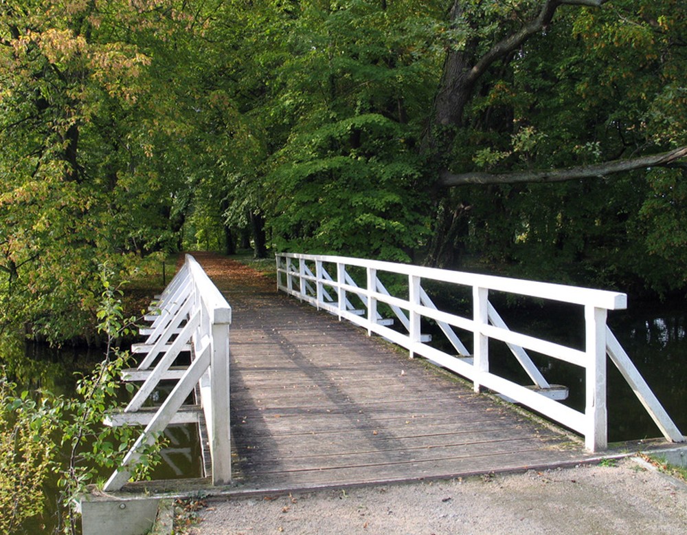 Am Schloss führt eine Brücke mit weißer Brüstung in den Park des Schlosses. Sie führt über die Gräfte der Anlage.