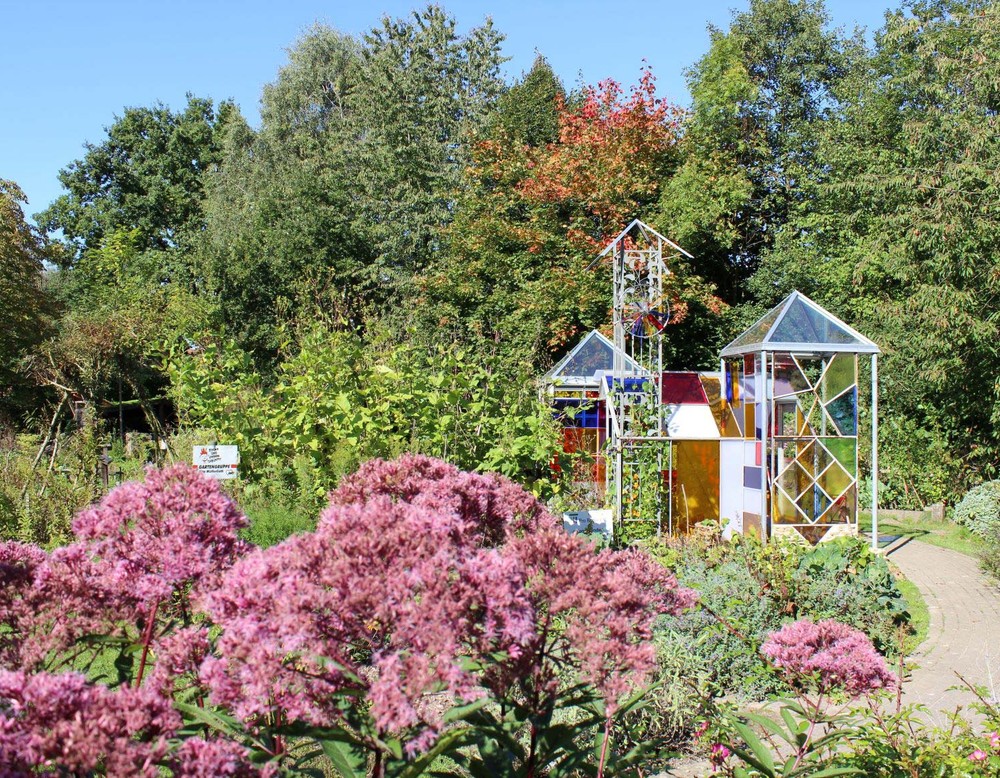 Blick auf den Schulgarten des Umweltzentrums Heerser Mühle. In dem Gewächshaus aus buntem Glas wachsen Kakteen.