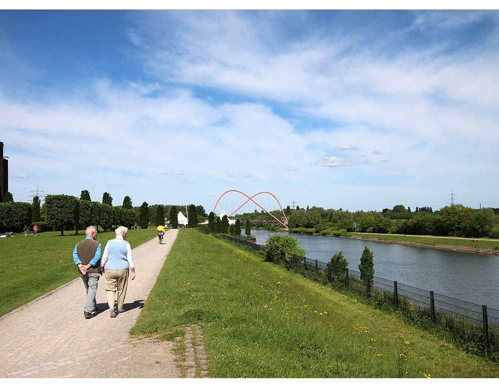 Weg am Rhein-Herne-Kanal. Der Kanal verläuft durch den Nordsternpark Gelsenkirchen. Im Hintergrund sieht man die Bogenbrücke.