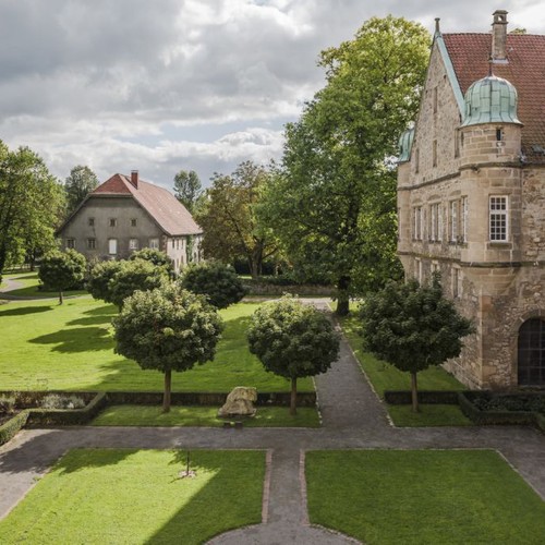 Innenhof des Klosters Willebadessen. Dieser ist von der Pfarrkirche St. Vitus, dem Konventsgebäude und der Abtei umgeben. Die offene Seite des Hofes ist mit Hecken und Bäumen bepflanzt.