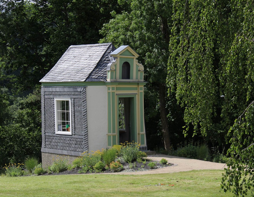 Das leicht schiefe klassizistische Gartenhaus "Twiete 6" in den Arnsberger Bürgergärten. Das Fachwerkhaus ist mit Naturschiefer beschlagen und ist großen Fenstern versehen.